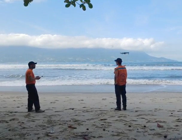 Buscas por Bruno Barreto Otsu em São Sebastião contam com drones, helicóptero Águia e apoio do GBMar A Defesa Civil de São Sebastião reforçou as buscas por Bruno Barreto Otsu, de 21 anos, desaparecido desde a última segunda-feira (11) após entrar no mar na costeira da praia de Toque-Toque Grande, na Costa Sul do município. A operação passou a contar com drones para monitoramento aéreo em áreas de difícil acesso. Para ampliar a área de monitoramento, a Defesa Civil passou a utilizar drones durante a operação. O equipamento permite alcançar pontos de difícil acesso, principalmente em locais atingidos por fortes ondas e mar agitado, onde a aproximação por terra ou embarcações é limitada. Segundo a Defesa Civil, a tecnologia auxilia no aumento do campo de visão das equipes e possibilita uma cobertura mais ampla da área marítima. O coordenador municipal da Defesa Civil, Ricardo Cardoso dos Santos, afirmou que o trabalho ocorre de forma integrada com outras forças de segurança e resgate da região. “Temos equipes preparadas, equipamentos e embarcações que podem contribuir nas buscas tanto pelo mar quanto nas costeiras. Estamos empenhados em apoiar todas as frentes da operação e esperamos que em breve possamos ter alguma notícia sobre o jovem”, declarou. Além das equipes terrestres e marítimas, a Polícia Militar também utiliza o Helicóptero Águia nas buscas aéreas pela região. De acordo com informações apuradas pelas equipes de resgate, Bruno entrou no mar para tentar salvar Maria Eduarda, também de 21 anos, após a jovem ser arrastada por uma onda enquanto caminhava pela costeira de Toque-Toque Grande. Maria Eduarda foi levada pela correnteza e encontrada cerca de cinco horas depois nas proximidades da praia de Barequeçaba, a aproximadamente cinco quilômetros do local inicial. Ela foi resgatada por um pescador que seguia em direção a Santos e acionou o Corpo de Bombeiros. Segundo relato prestado pela jovem aos bombeiros marítimos, Bruno não foi atingido diretamente pela onda, mas entrou na água na tentativa de ajudá-la e desapareceu em seguida. Familiares de Bruno Barreto Otsu também mobilizam campanhas nas redes sociais em busca de apoio voluntário para auxiliar nas buscas. Os pedidos envolvem proprietários de embarcações, mergulhadores e operadores de drones.  